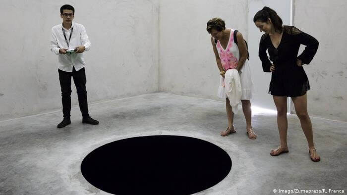 Three people observing a hole in the floor